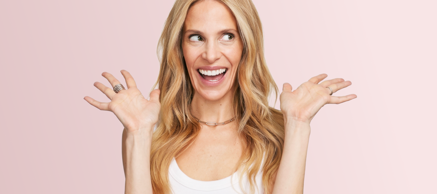 Dr. Marnie smiling with a delighted expression on a pink background — founder excitement for the skincare line.