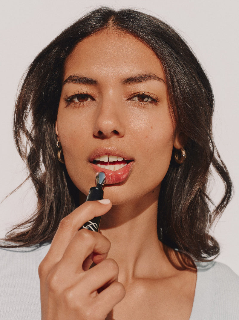 Model applying Dr. Marnie Lip Serum with the cooling metal applicator — a clinical-grade plumping treatment.
