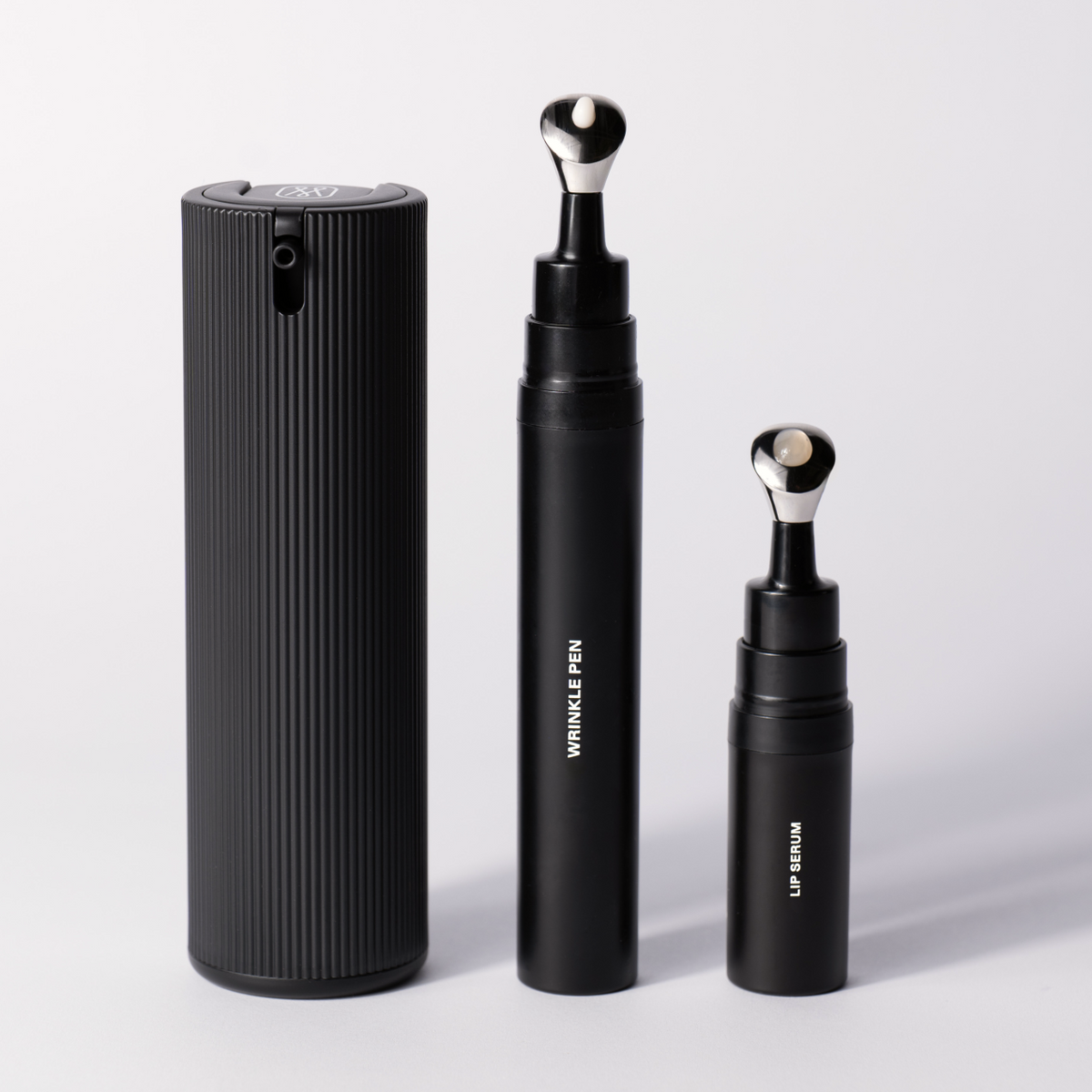 Packshot of all three Essential Collection products: the ribbed Facial Serum bottle, the Wrinkle Pen and the Lip Serum, standing side by side.