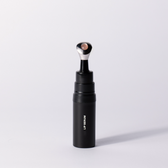 The black Lip Serum applicator standing upright with its pink-tipped applicator on a soft white studio background.