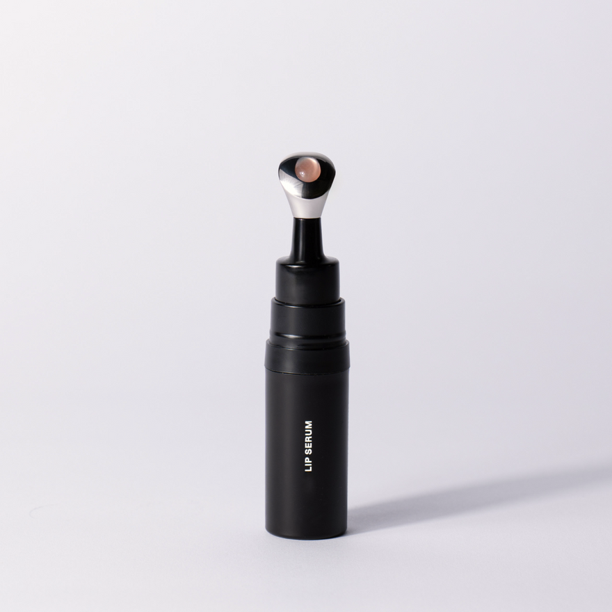 The black Lip Serum applicator standing upright with its pink-tipped applicator on a soft white studio background.