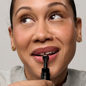 A smiling model applying the Lip Serum applicator to her lower lip.