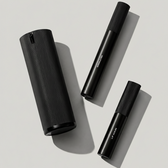 Packshot of all three Essential Collection products — the ribbed Facial Serum bottle, Wrinkle Pen and Lip Serum — arranged on a plain warm-grey background with cast shadows