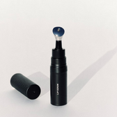 The black Lip Serum applicator bottle standing upright with its ribbed cap lying beside it on a plain pale grey background
