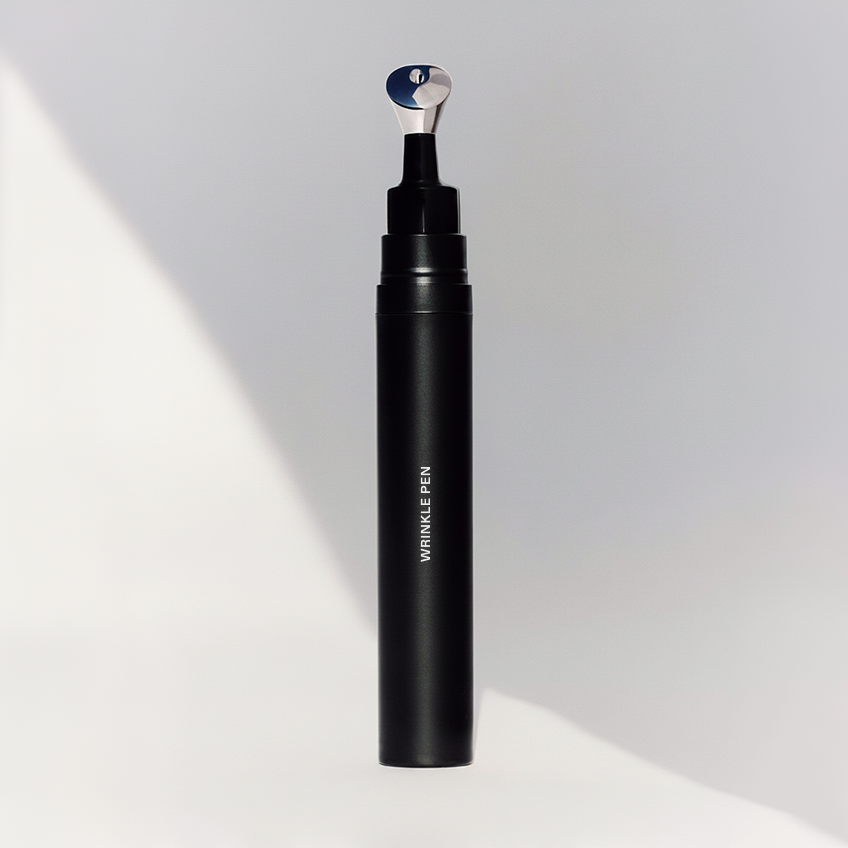 The black Wrinkle Pen standing upright with its metal applicator tip exposed, on a plain grey background with a diagonal shadow