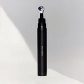 The black Wrinkle Pen standing upright with its metal applicator tip exposed, on a plain grey background with a diagonal shadow